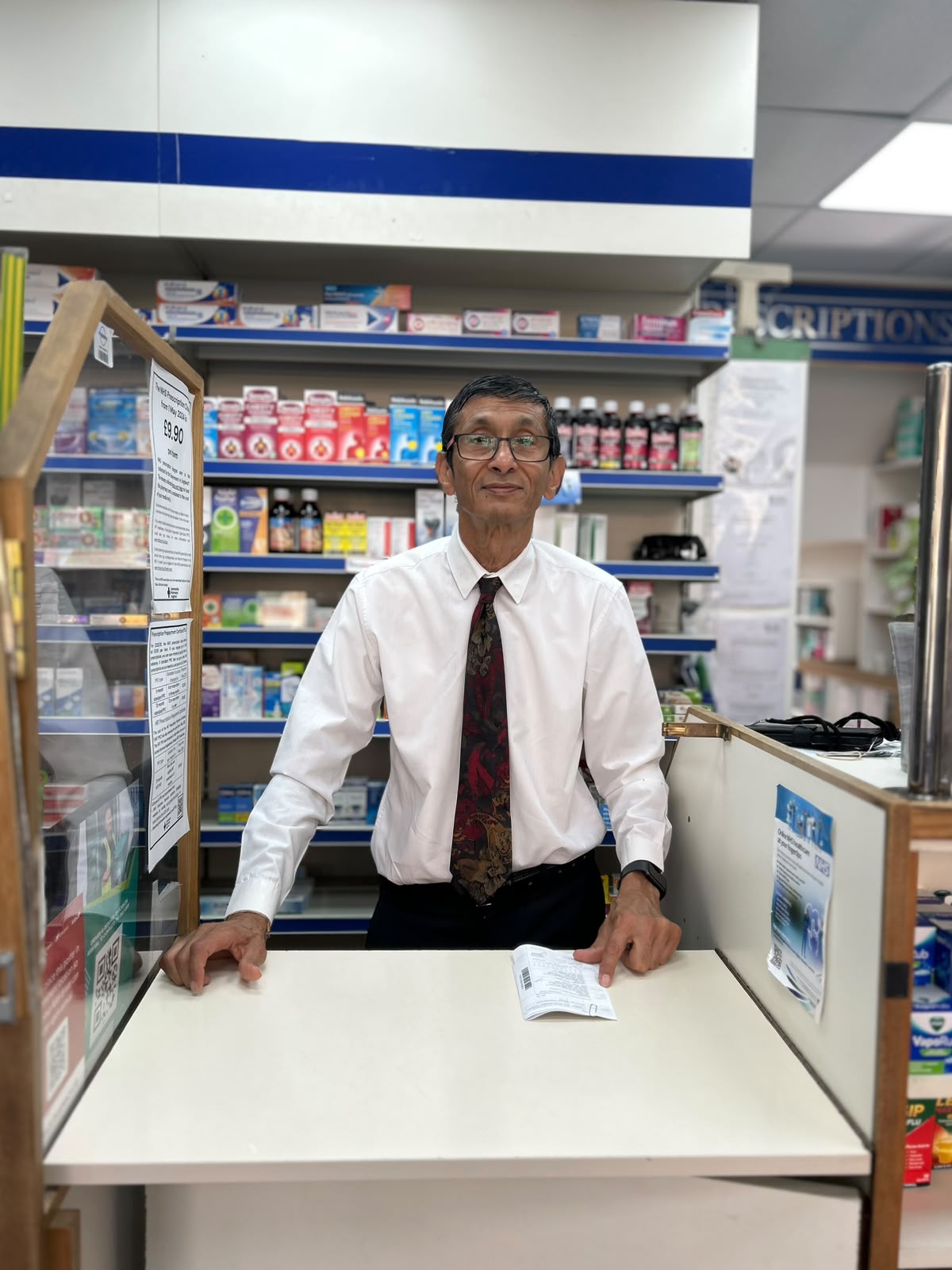 The pharmacist at Saigrace Pharmacy standing at the prescriptions counter, ready to offer health advice